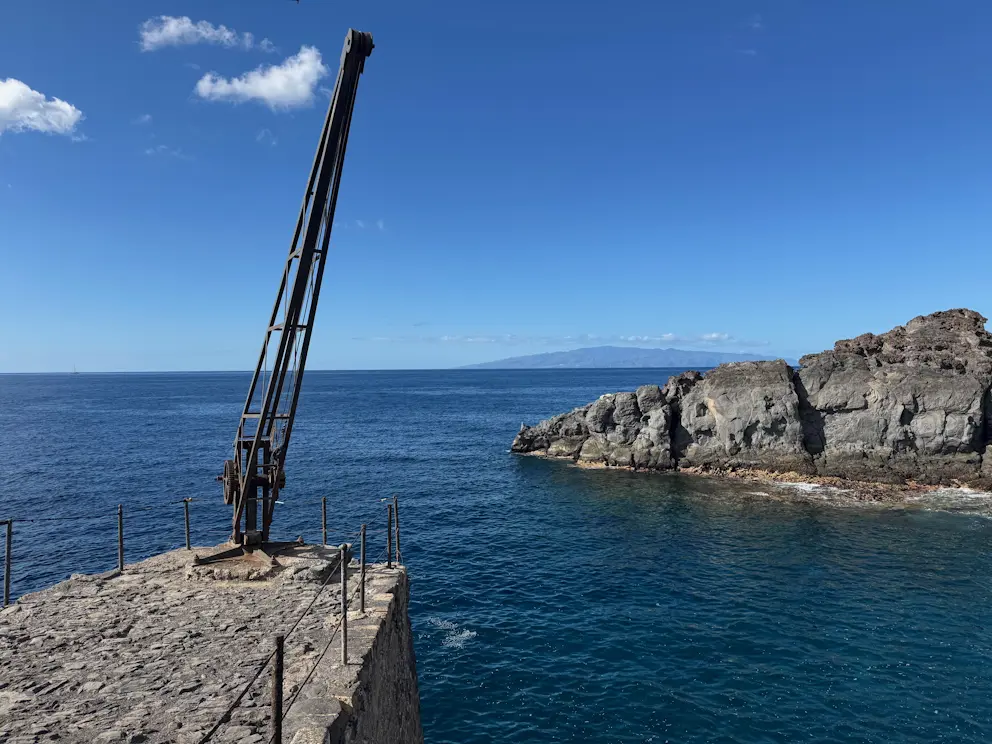 Zabytkowy dźwig portowy na molu, w tle wulkaniczne skały